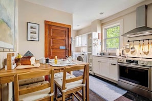 A modern kitchen with a wooden dining table, white cabinets, and stainless steel appliances. - Classic charm with modern comforts near Harvard. (Cambridge)