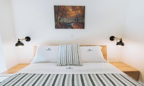 A bed with two pillows, a striped blanket, and a painting of a river scene above it. - Rhodes Port Haven Suite (Rhodes)