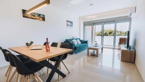 A modern living room with a wooden dining table, black chairs, a blue sofa, and a small coffee table. - Rhodes Port Haven Suite (Rhodes)