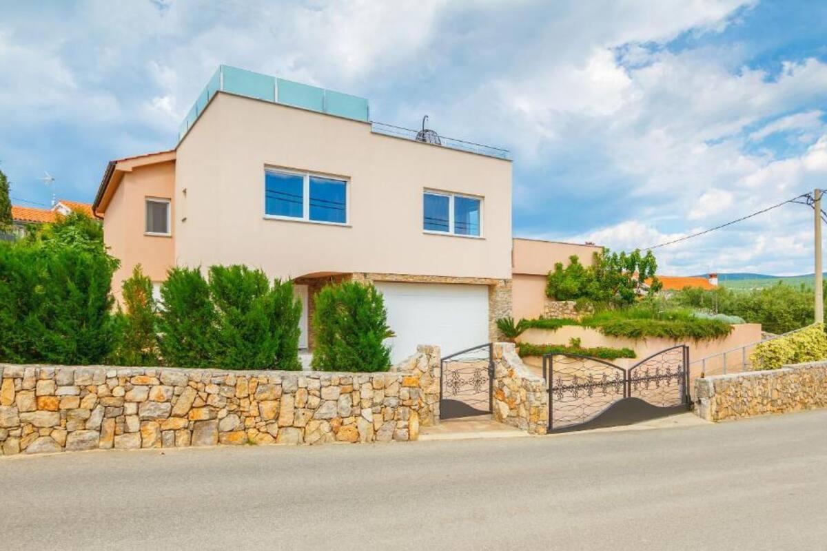 A modern two-story house with a stone wall entrance, a garage, and a clear sky.