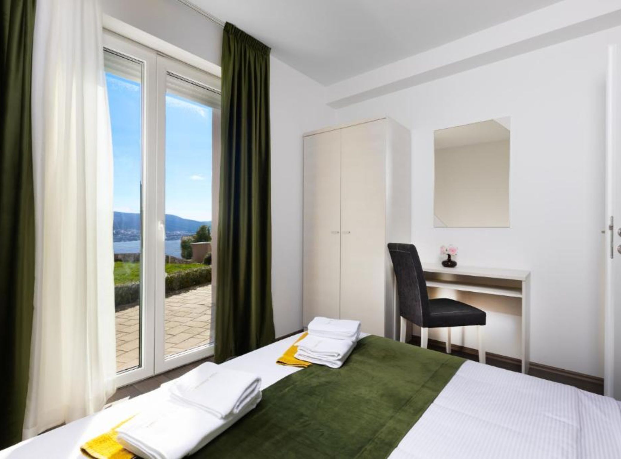 A hotel room with a bed, a desk, a chair, and a view of the outdoors.