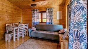 A wooden cabin interior with a sofa, dining table, chairs, and curtains. - Holiday Homes With Terraces, Sauna + Whirlpool (gmina Będzino)