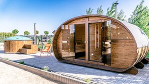 A modern, wooden, semi-circular building with large glass doors, a small adjacent wooden structure, and a paved area with a bench. - Holiday Homes With Terraces, Sauna + Whirlpool (gmina Będzino)