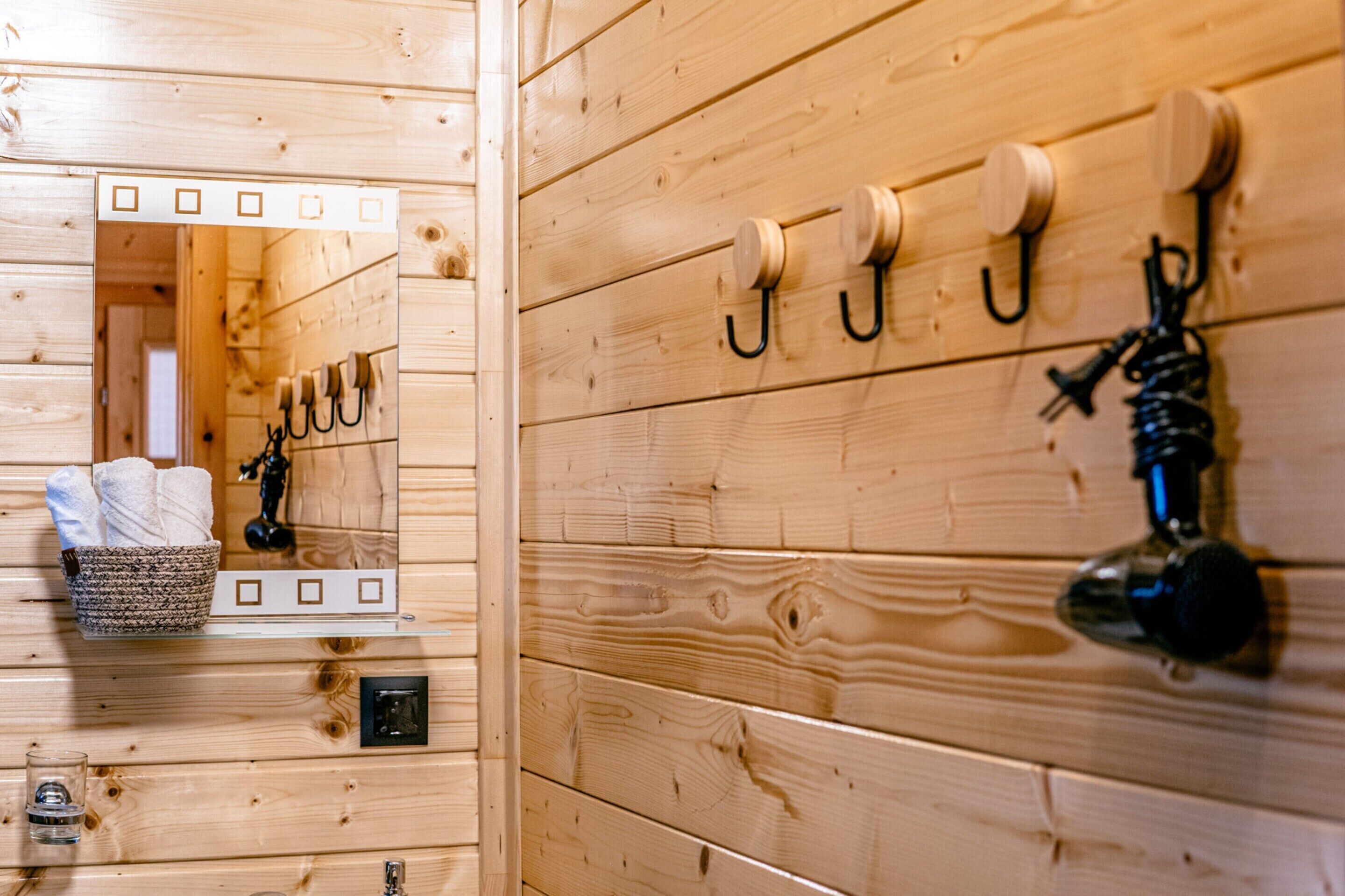 Interior de madera con un espejo, ganchos para colgar objetos y un estante con toallas y una cesta.