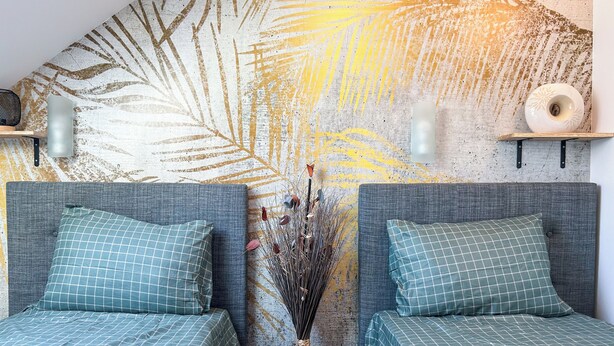 A room with two beds, each with a grey headboard and teal bedding. There is a decorative vase with dried plants in the center, and a textured wall with a leaf pattern. - Room N3 Colocation Confort & Service (91) (Saint-Pierre-du-Perray)