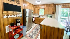 A compact kitchen with wooden cabinets, a stainless steel refrigerator, a microwave, and a coffee maker. - Smoky Mountain Creekside Retreat - Private Cabin with Backyard Stream (Maggie Valley)