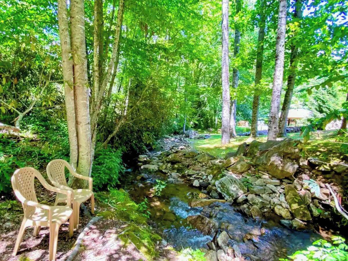 A natural setting with a stream, trees, and two plastic chairs.