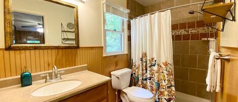 Un baño con tocador de madera, un lavamanos blanco, un inodoro y una ducha con cortina floral.