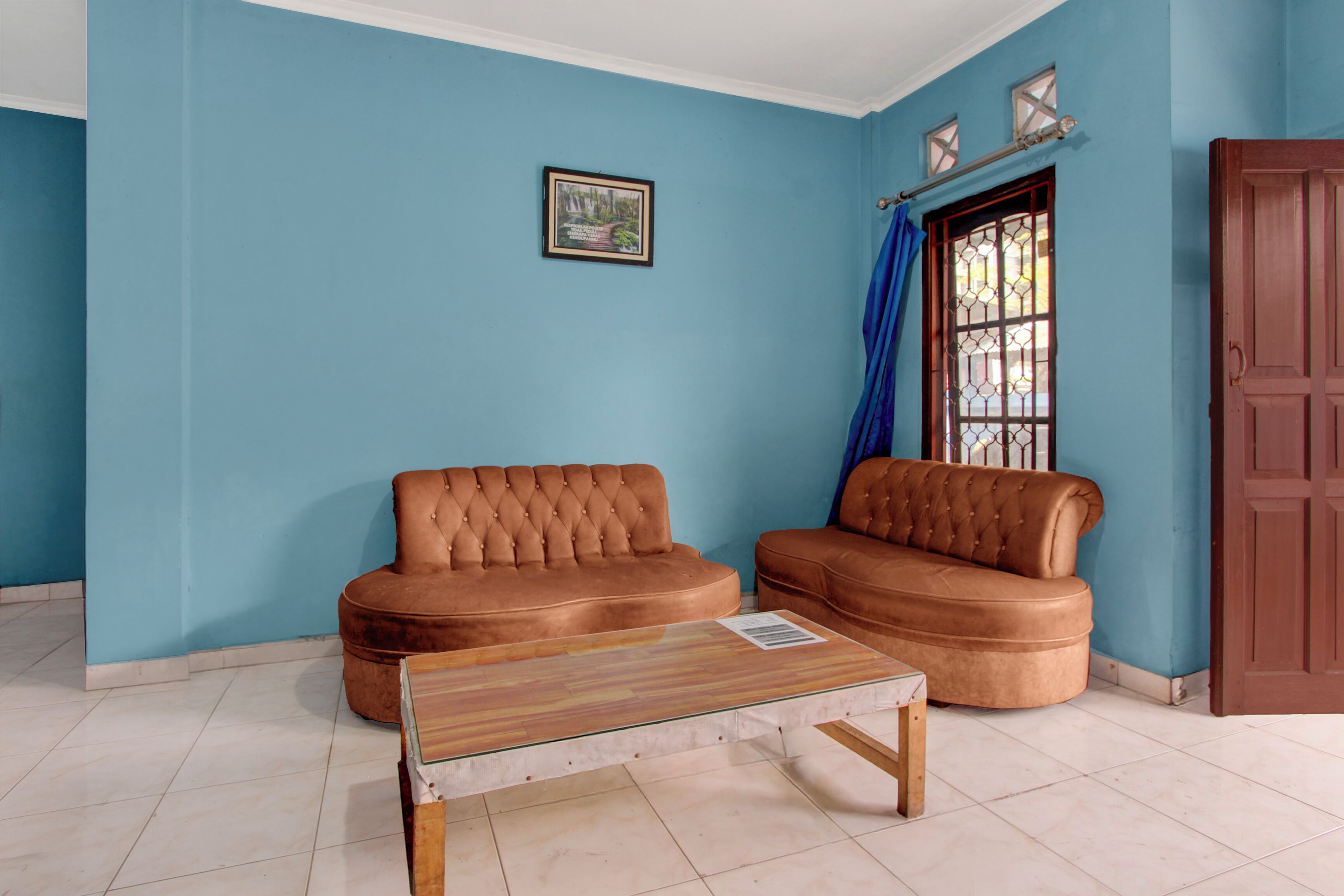 A room with two brown sofas, a wooden coffee table, a window with blue curtains, and a door.