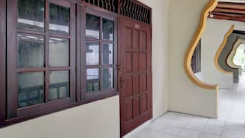 Un couloir avec une grande porte en bois et une fenêtre ornée d’une grille métallique.