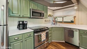 A kitchen with green cabinets, a stainless steel refrigerator, a microwave, a stove, and a coffee maker. - Treetop Lakehouse at Abbey Springs (Fontana-on-Geneva Lake)
