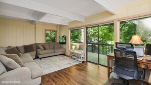 A living room with a sectional sofa, a desk with a computer, and a balcony with a view of trees. - Treetop Lakehouse at Abbey Springs (Fontana-on-Geneva Lake)