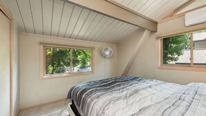 A bedroom with a sloped ceiling, a bed with a striped comforter, a window with a view of trees, and a ceiling fan. - Treetop Lakehouse at Abbey Springs (Fontana-on-Geneva Lake)