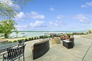 Um pátio externo com móveis de vime, lareira e vista para o lago e marina.