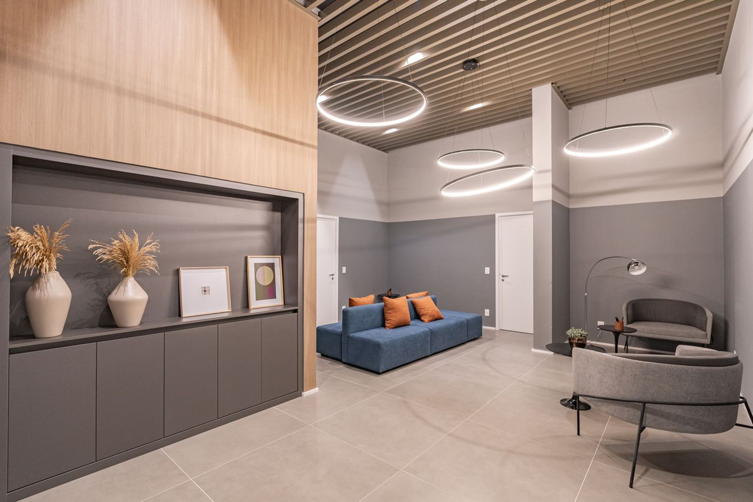 Un interior moderno con un sofá, una silla, un panel de pared de madera y una estantería con objetos decorativos.