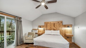 A bedroom with a wooden headboard, a bed, a bench, a chair, and a view of the outdoors.