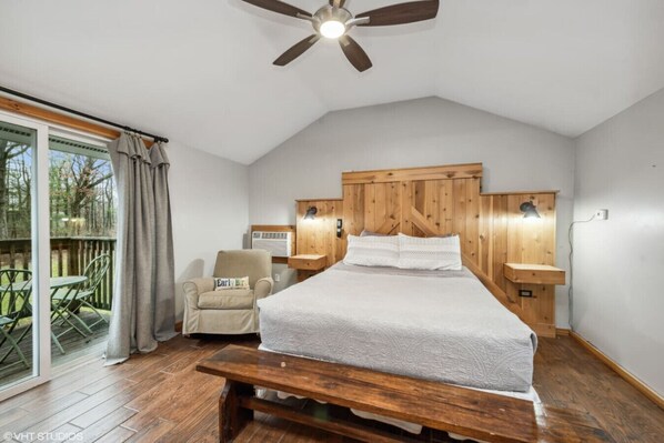 A bedroom with a wooden headboard, a bed, a bench, a chair, and a view of the outdoors.