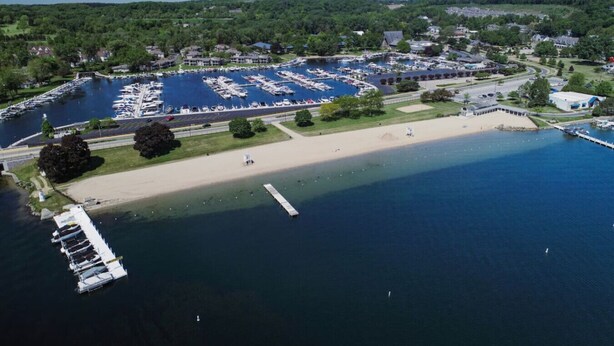 An aerial view of a marina with multiple docks and boats, a sandy beach, and surrounding greenery.
