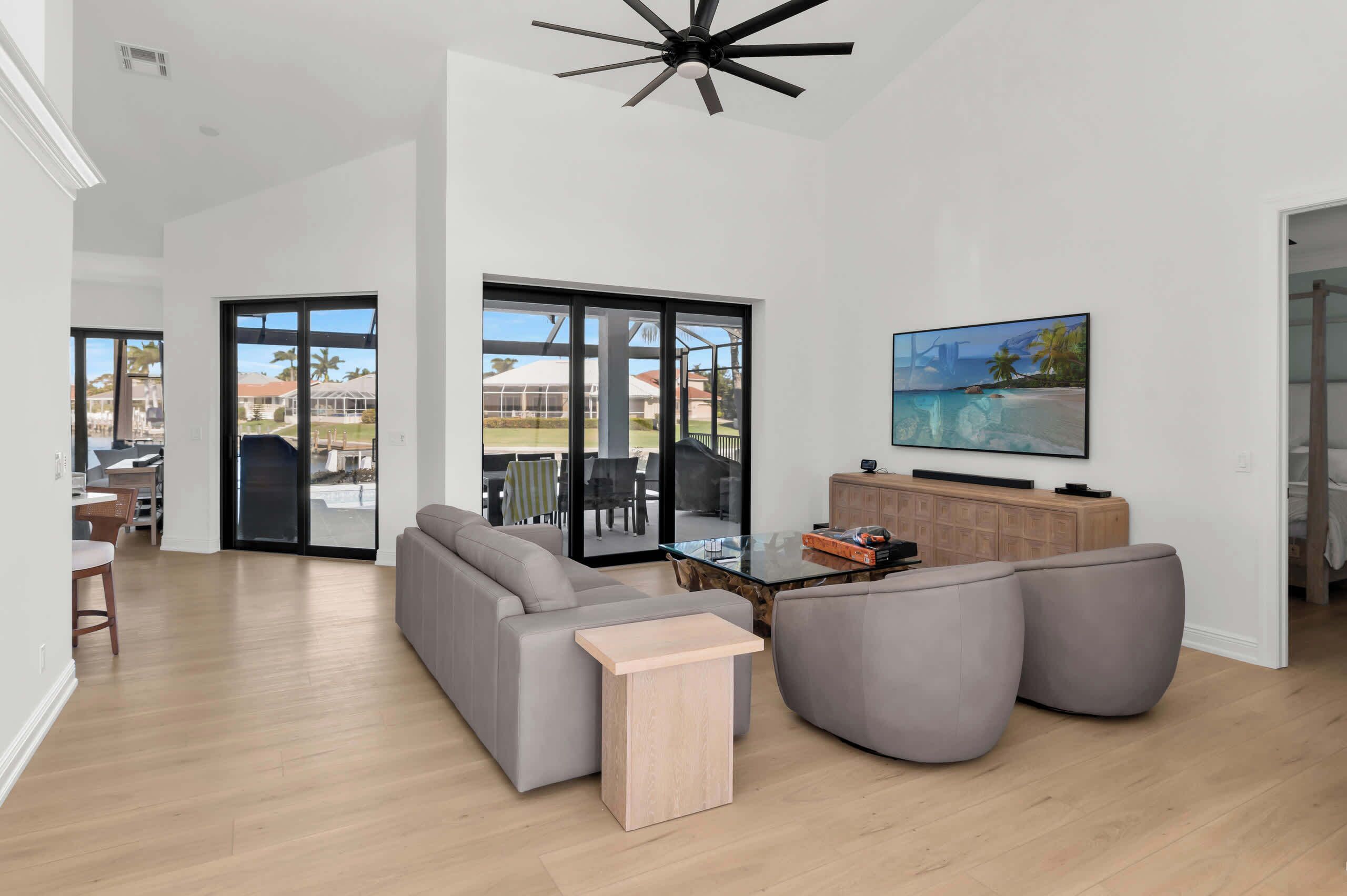A modern living room with a grey sofa, a glass coffee table, and a ceiling fan.