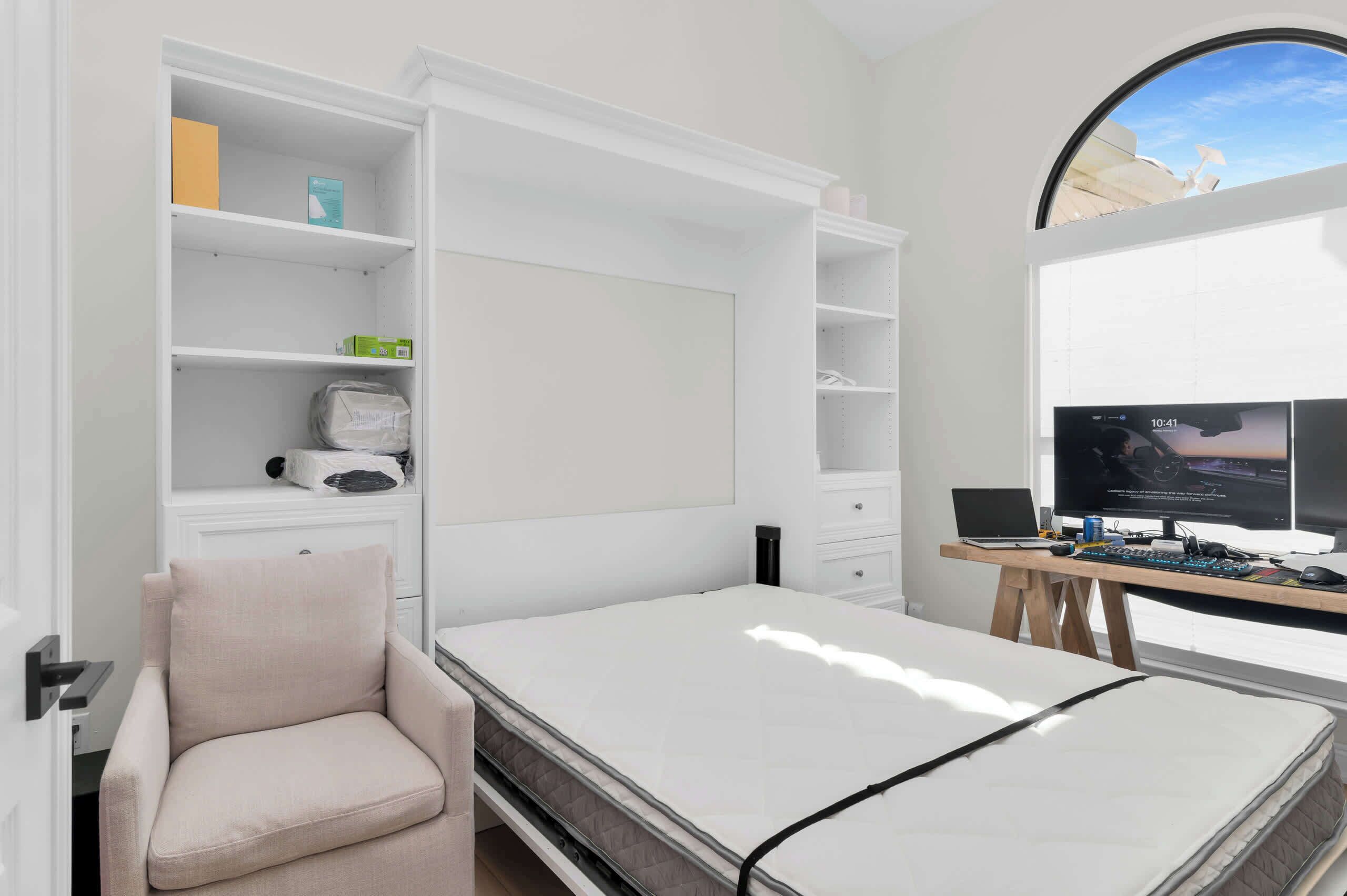 A bedroom with a bed, a chair, a desk with a computer, and a TV.