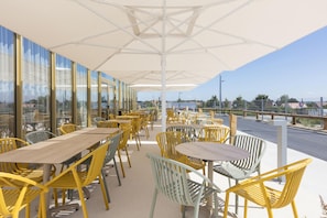 Un espace extérieur aménagé avec des tables et des chaises, de grands parasols et une vue sur le paysage urbain.