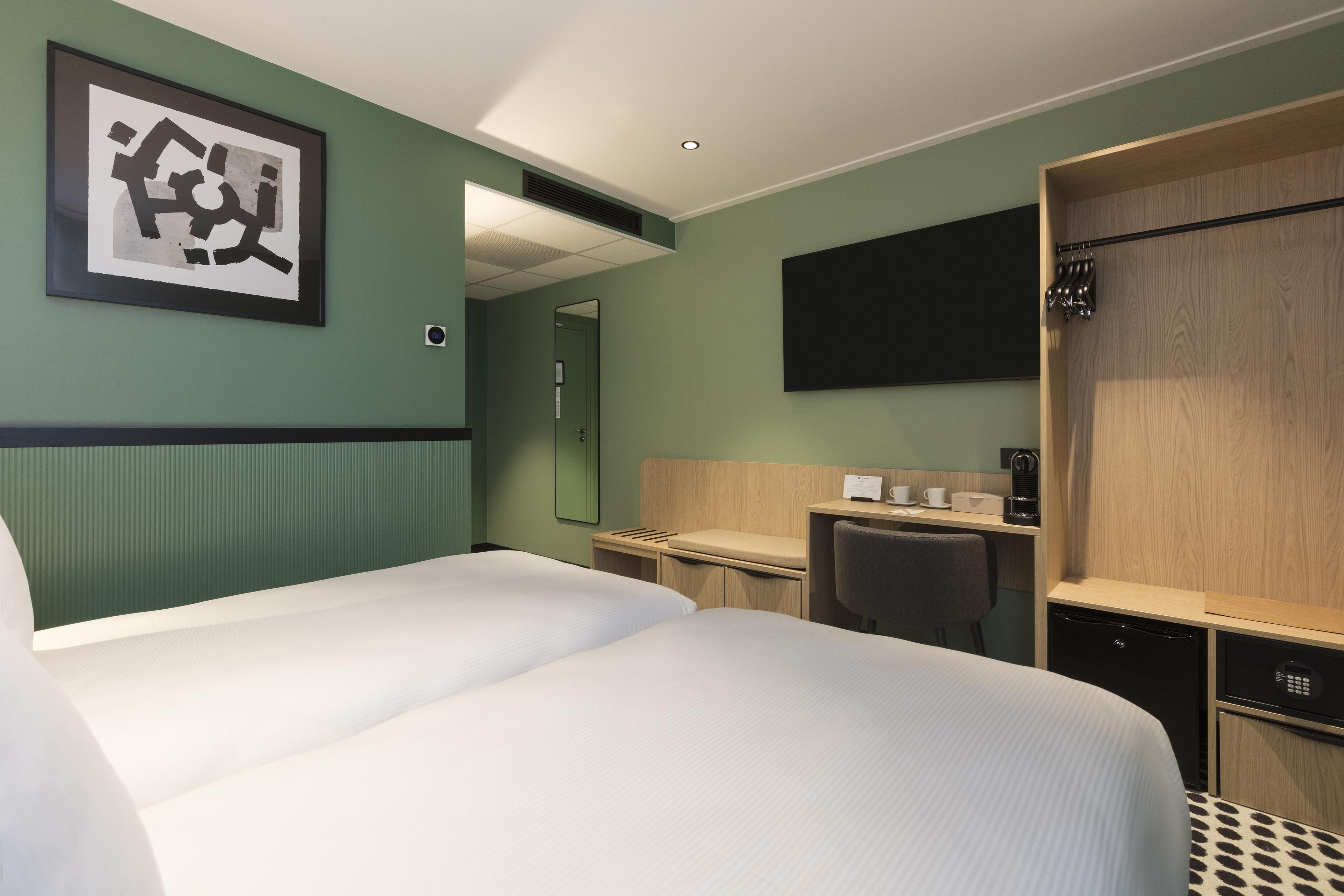 Une chambre d’hôtel équipée d’un lit, d’un bureau, d’une chaise, d’un miroir, d’une télévision et d’une armoire.