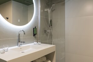 A modern bathroom with a large mirror, a shower, and a sink with two glasses.