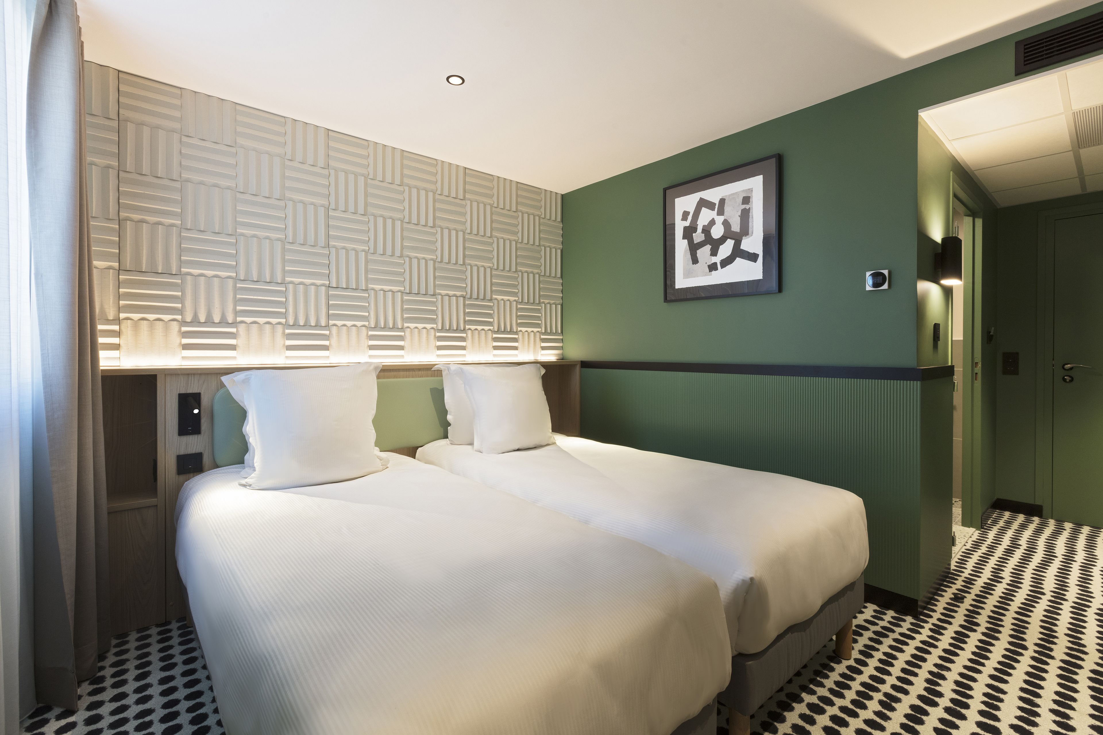 Habitació d'hotel amb dos llits, un panell de capçaleri amb disseny, una obra d'art emmarcada a la paret i un paviment estampat.