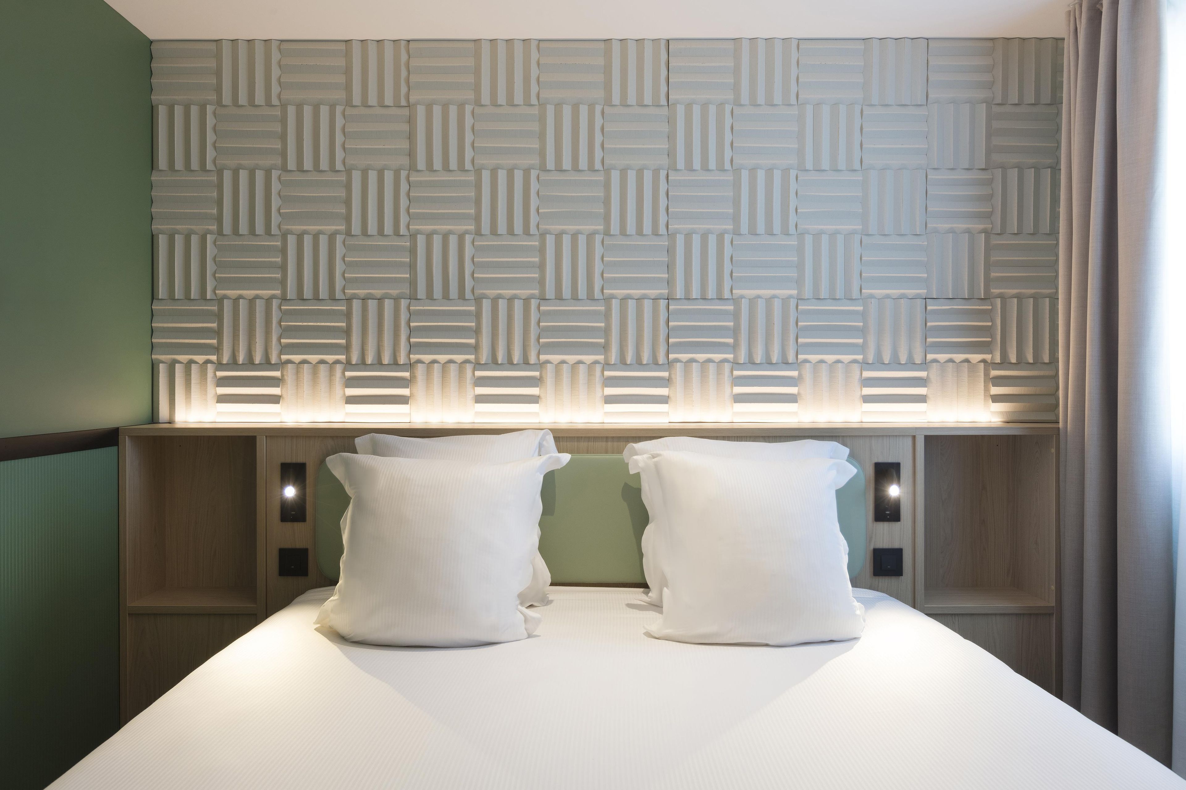 Habitación de hotel con cabecera estampada, dos almohadas y mesita de noche con lámpara.