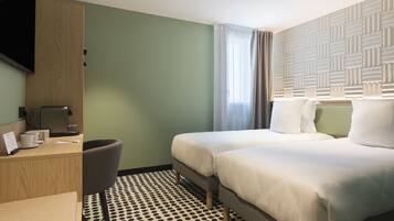 Una habitación de hotel con cama, escritorio, silla, televisor y piso estampado.
