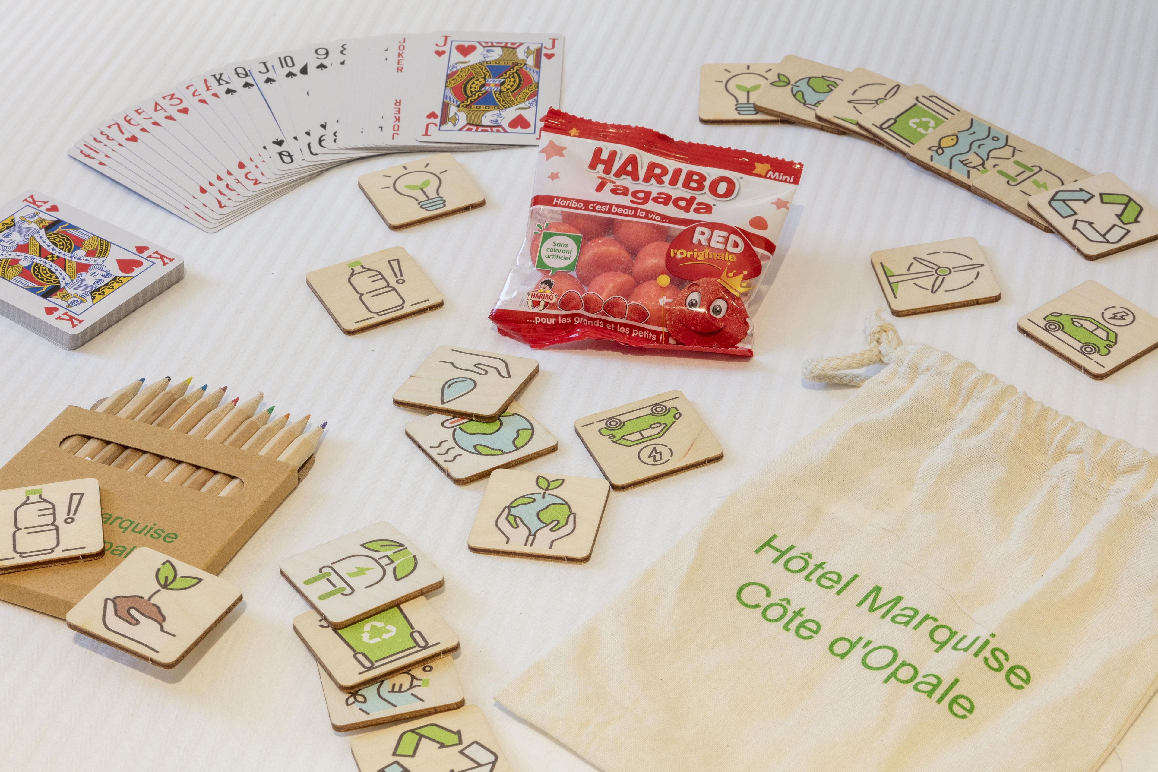 Kokoelma puisia aluslaseja, joissa on kierrätysmerkkejä, paketti Haribo Targada -karkkeja ja pussi, jossa on teksti ”Hôtel Marquise Côte d’Opale”.