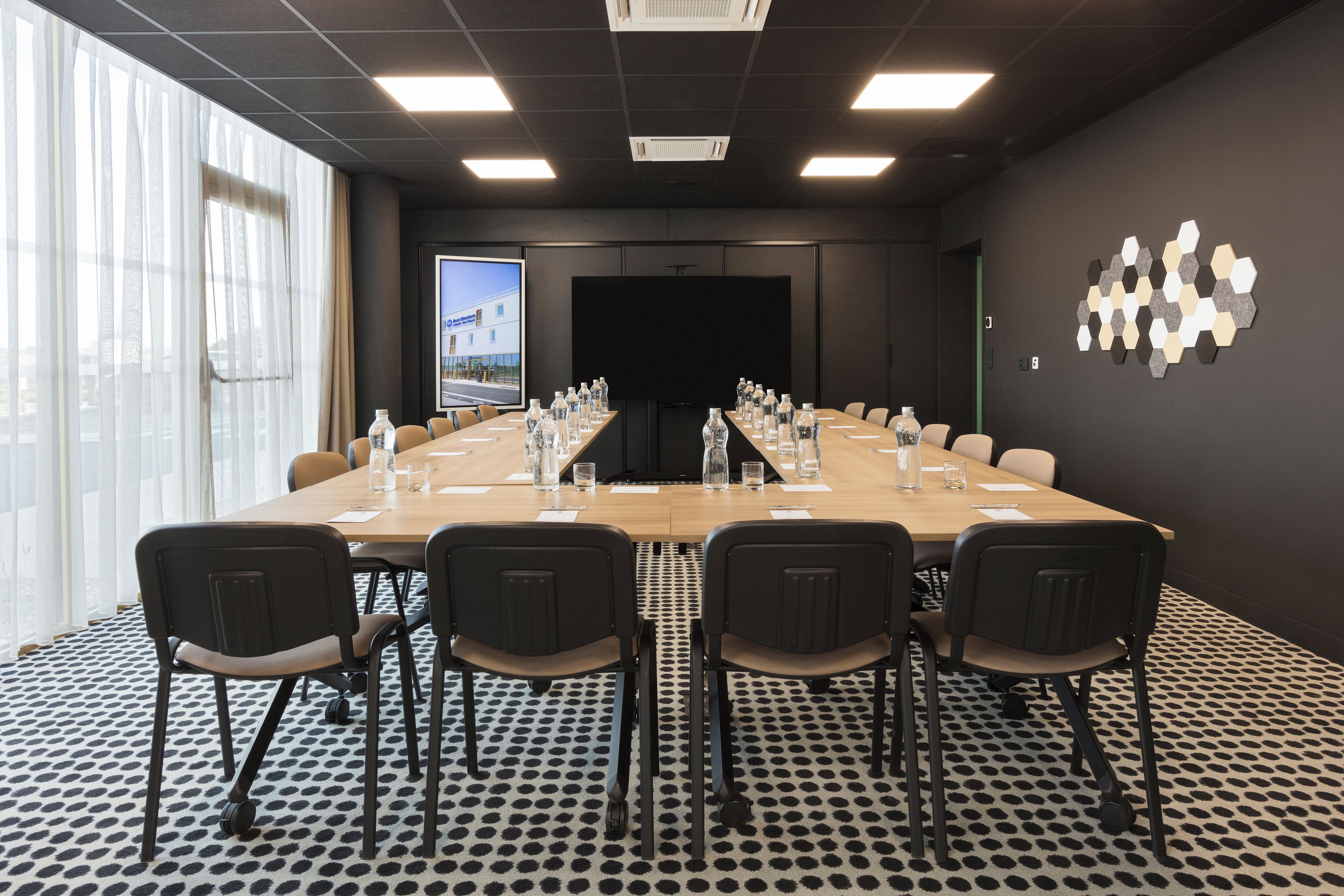 Een vergaderruimte met een lange tafel, stoelen, een projectiescherm en een groot raam.