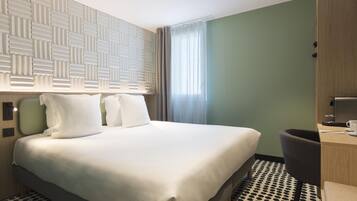 A hotel room with a large bed, a desk with a chair, a wardrobe, and a window with curtains.