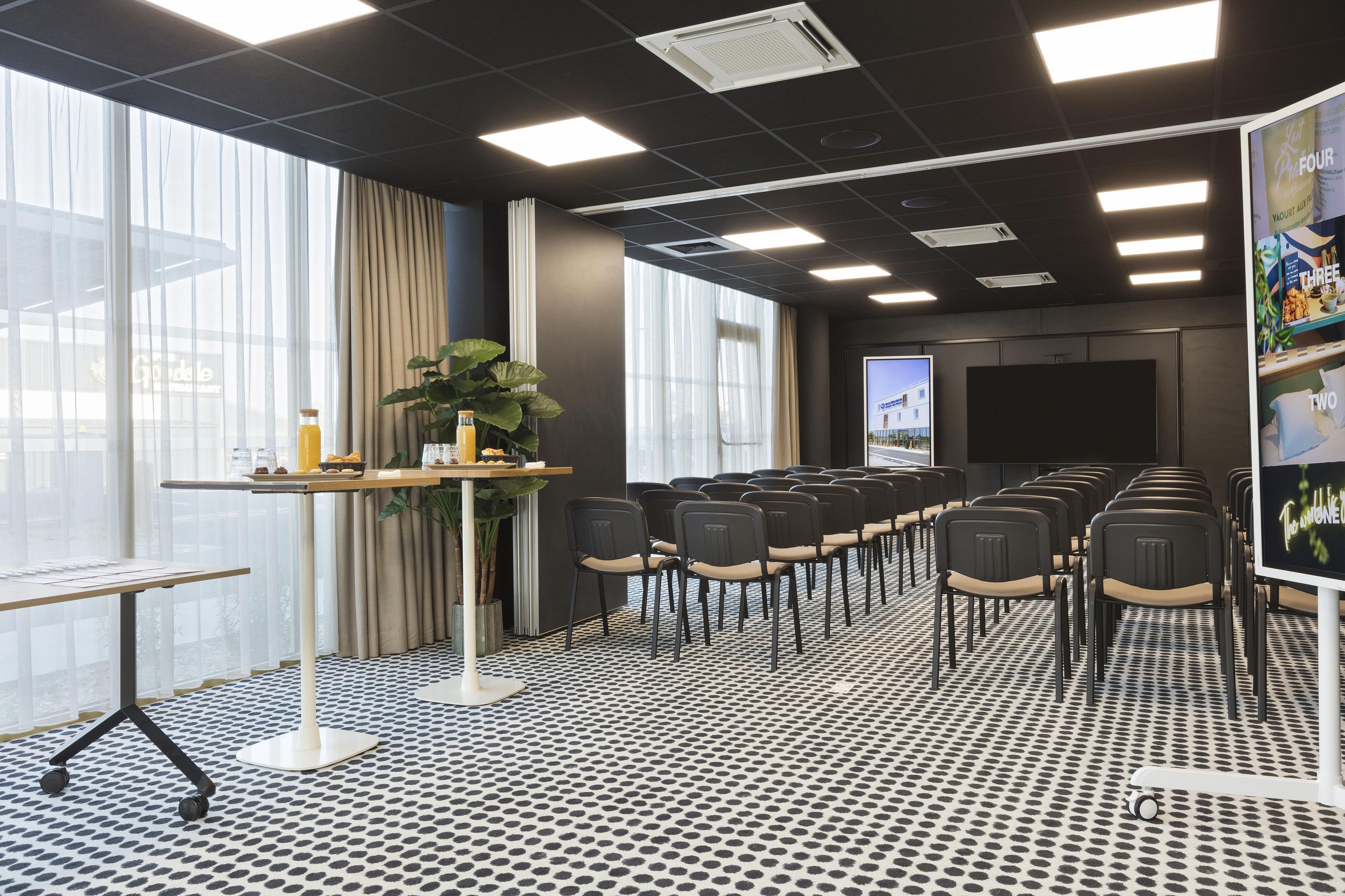 Un salón de conferencias con una larga mesa, sillas, una pantalla de proyector y un amplio ventanal con cortinas.