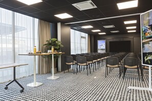 Une salle de conférence avec une longue table, des chaises, un écran de projection et une grande fenêtre avec des rideaux.