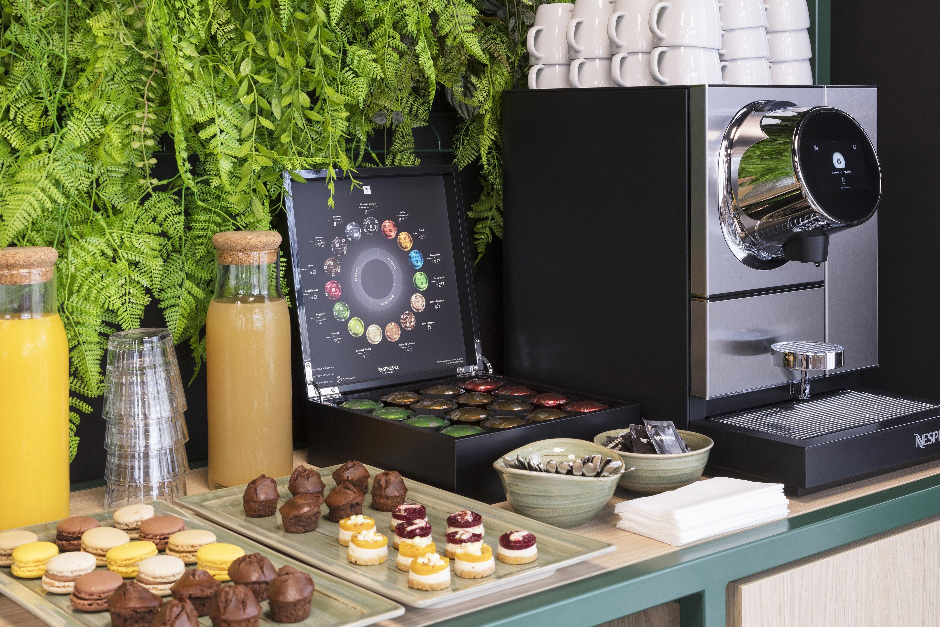 A coffee station with a Nespresso machine, a variety of coffee pods, and a selection of pastries.