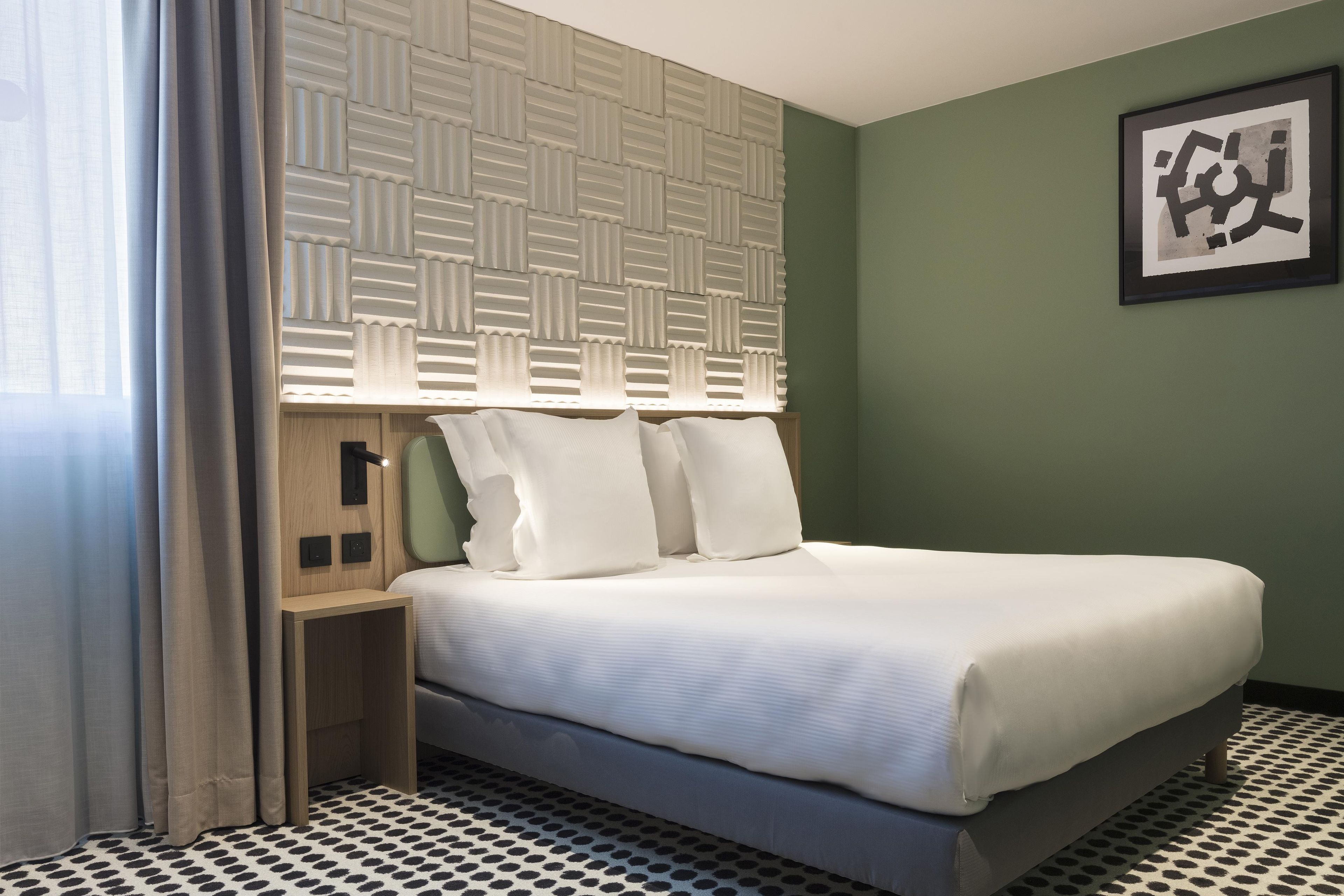 Habitació d'hotel amb un llit, un capçal amb dibuixos geomètrics, una taula de nit i un quadre encimbellat a la paret.