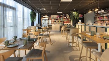 Een restaurantinterieur met meerdere eettafels en stoelen, een bar met flessenplanken en een koelkast op de achtergrond.