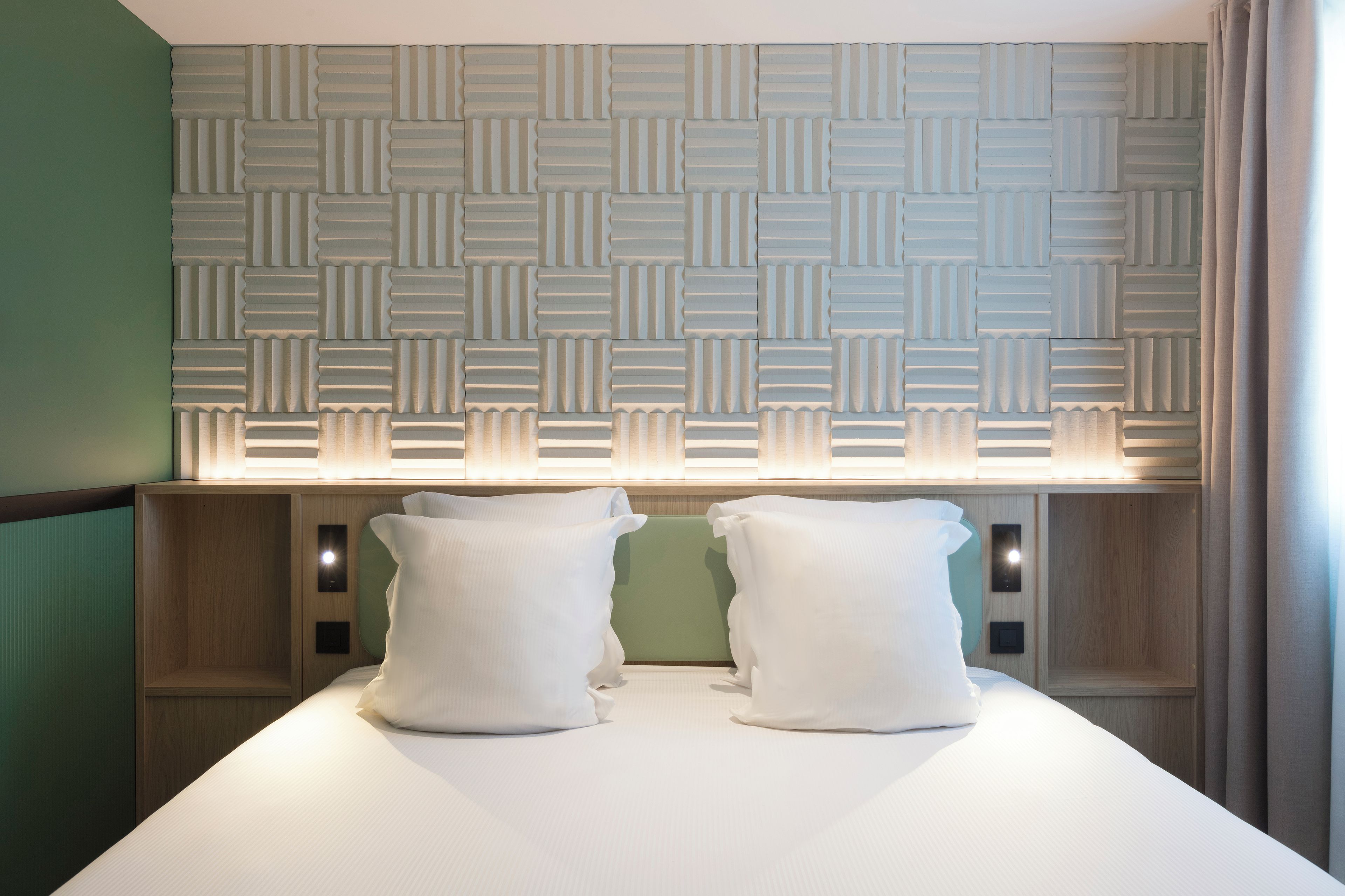 Una habitación de hotel con cabecera estampada, dos almohadas y una mesita de noche.