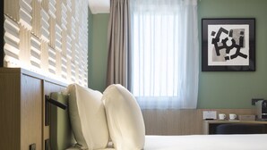 Habitación de hotel con cama, escritorio, cafetera y un cuadro en la pared.