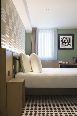 Une chambre d’hôtel avec un lit, un bureau, une machine à café et un mur orné d’un tableau.