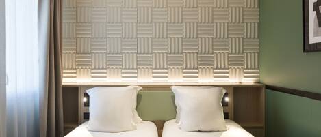 A hotel room with a bed, a window with curtains, a wall with a geometric pattern, and a framed picture on the wall.
