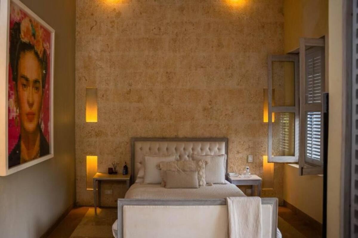 Une chambre à coucher avec un grand lit, une table de chevet, une lampe fixée au mur et un tableau.