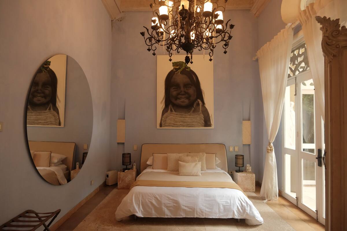 Une chambre à coucher avec un grand lit, un lustre, un miroir et une grande fenêtre avec des rideaux.