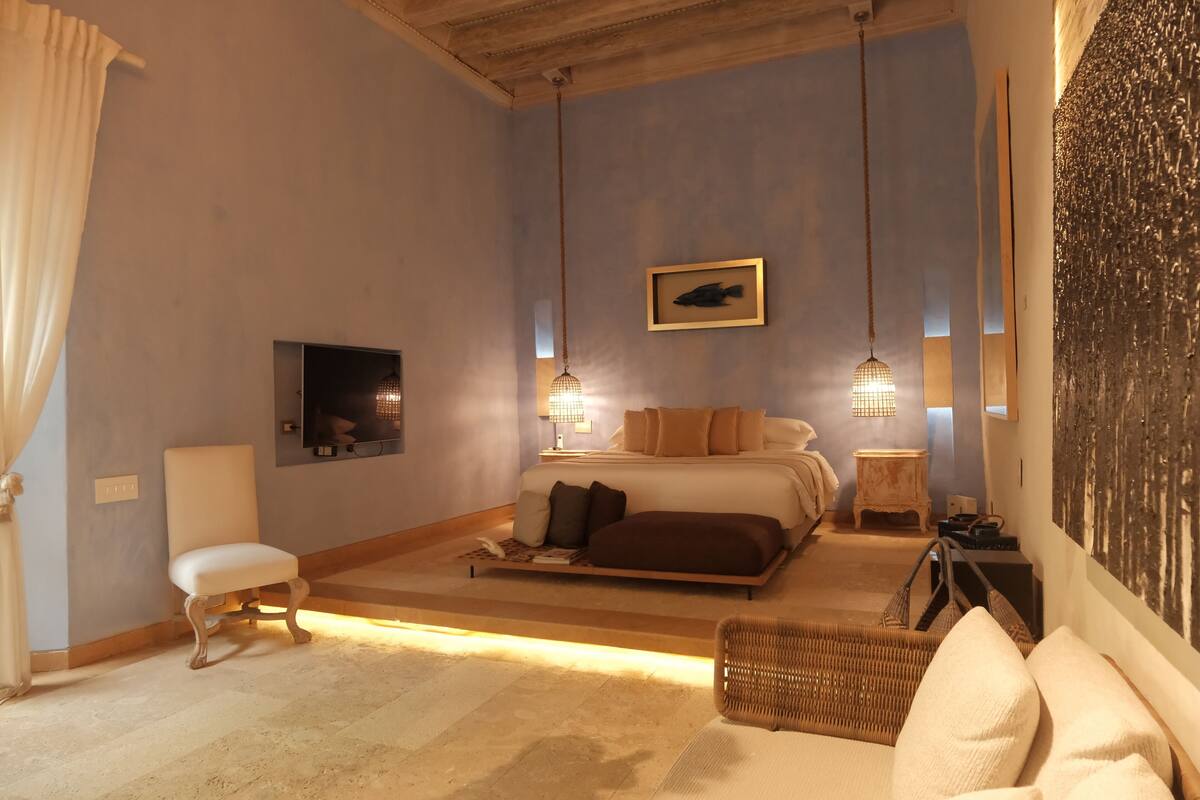Une chambre à coucher comprenant un lit, des tables de chevet, une chaise et une œuvre d’art accrochée au mur.
