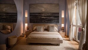 A bedroom with a large bed, a wall-mounted painting of the sea, bedside lamps, and a window with curtains. - Hotel Casa Santiago Botero (Cartagena)