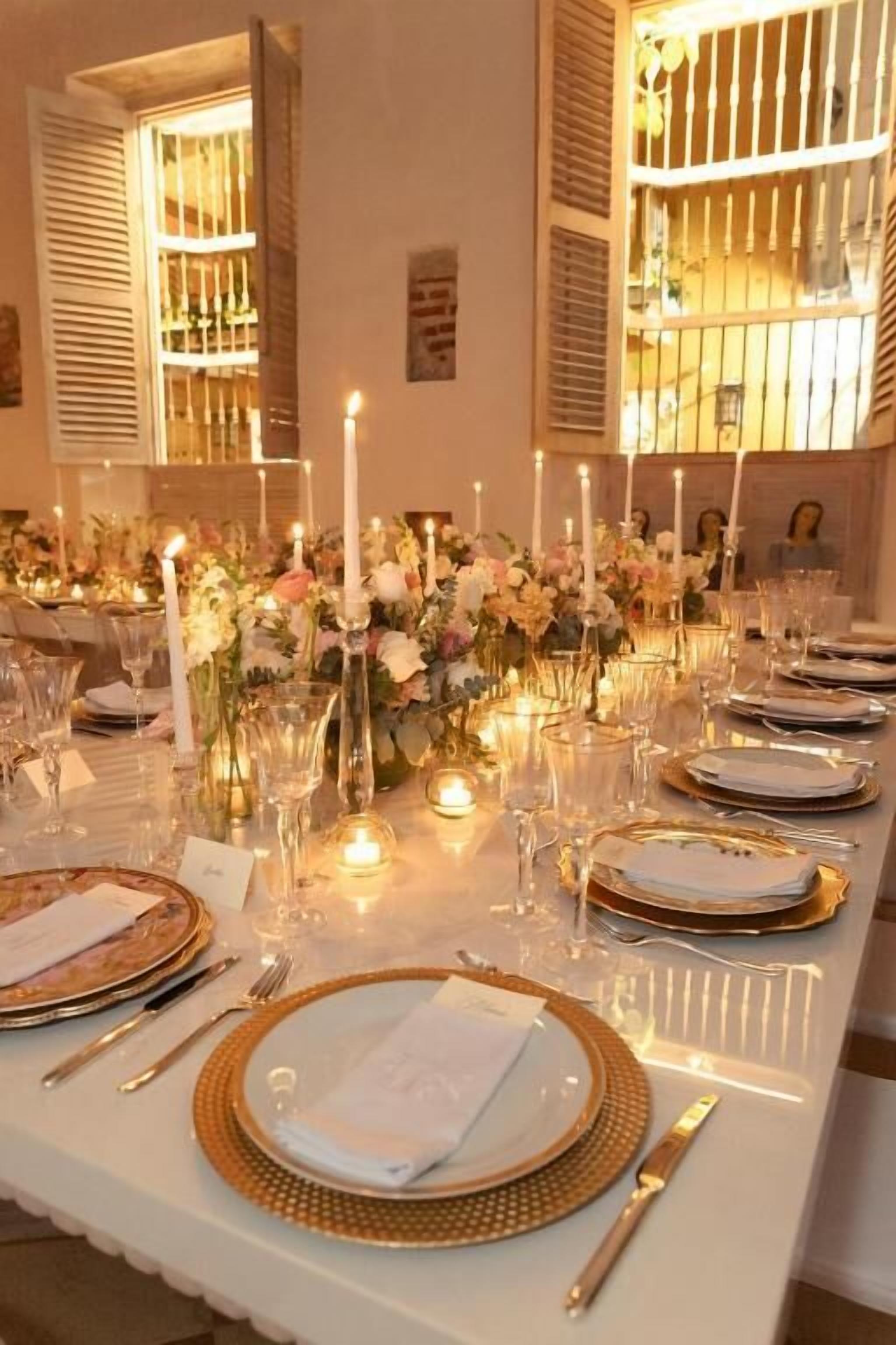 Ein langer Esstisch, festlich gedeckt für eine formelle Veranstaltung, mit Kerzen, floralen Mittelpunkten und elegantem Geschirr.