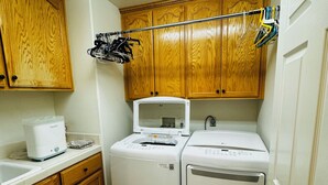A compact laundry room with wooden cabinets, a washing machine, a dryer, and a clothes drying rack. - 2 separate bedroom private bathroom 20 mins from Disneyland btw LA, and OC (Artesia)