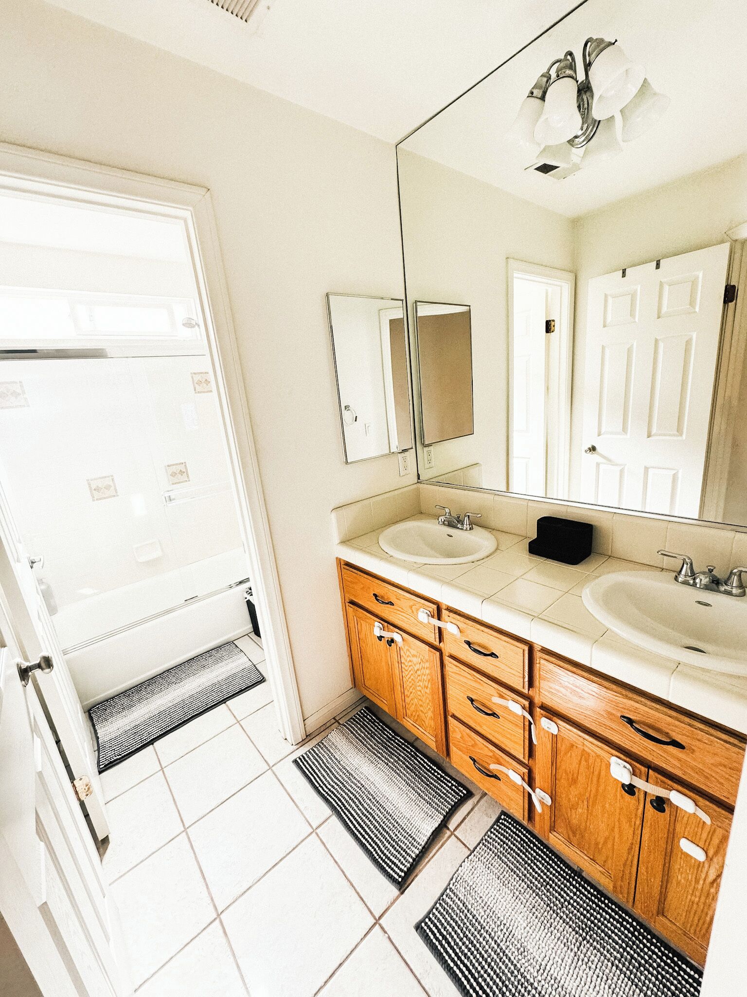 Un baño con dos lavamanos, armarios de madera, un espejo grande y una puerta que da a otra habitación.