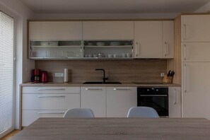 A modern kitchen with white cabinets, a wooden countertop, a black sink, and a built-in oven. - Bright apartment with balcony and mountain view (Bled)